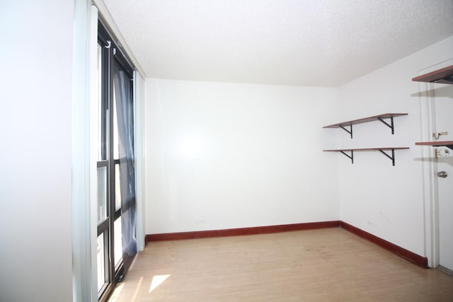 empty room featuring a textured ceiling, light wood finished floors, and baseboards