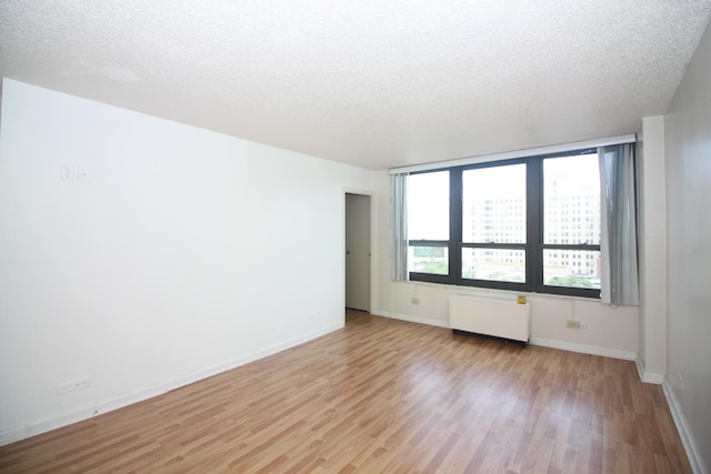 unfurnished room featuring light wood-type flooring, radiator heating unit, and a textured ceiling