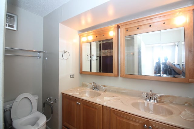 full bathroom featuring toilet, a textured ceiling, double vanity, and a sink