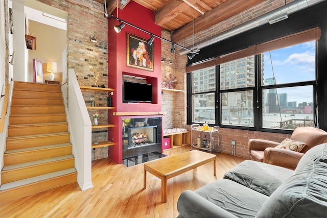 living area featuring a tile fireplace, wooden ceiling, brick wall, wood finished floors, and stairs