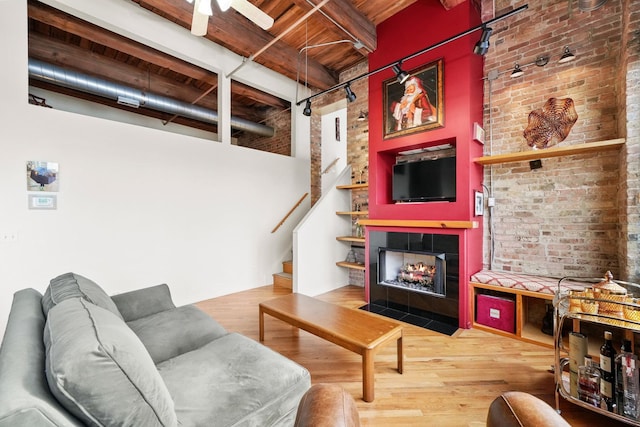 living area featuring a tile fireplace, a towering ceiling, brick wall, stairway, and wood finished floors