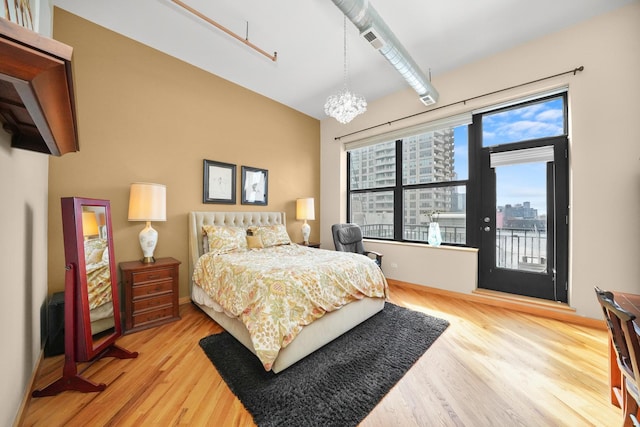 bedroom with a notable chandelier, a city view, baseboards, access to outside, and light wood-type flooring