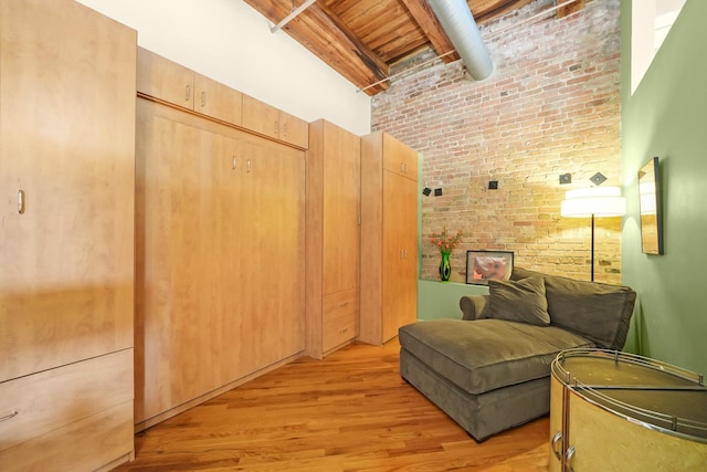 living area with brick wall, light wood finished floors, a high ceiling, and beam ceiling