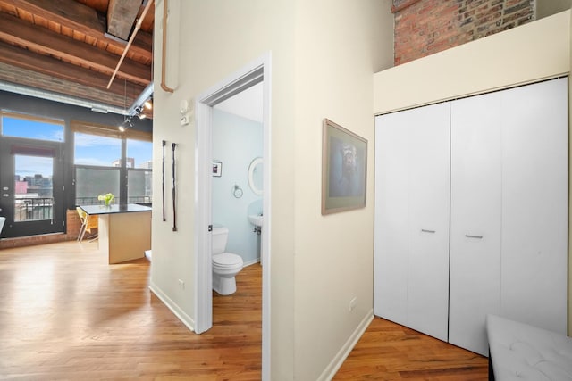 hall featuring light wood-type flooring, beamed ceiling, a towering ceiling, and baseboards