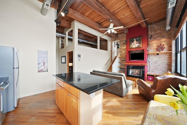 kitchen featuring a warm lit fireplace, light brown cabinets, a kitchen island, open floor plan, and appliances with stainless steel finishes