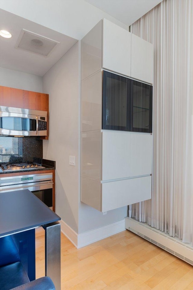 kitchen featuring light wood-style flooring, a baseboard heating unit, appliances with stainless steel finishes, decorative backsplash, and baseboards