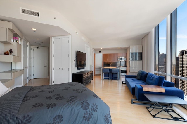 bedroom featuring a wall of windows, visible vents, light wood-style floors, and recessed lighting