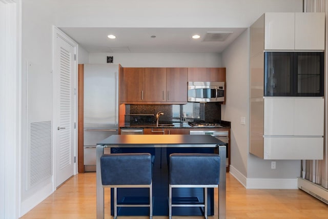 kitchen with backsplash, stainless steel appliances, light wood-style floors, and a sink