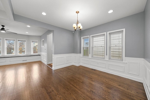 empty room featuring dark wood-style flooring, a wainscoted wall, recessed lighting, visible vents, and ceiling fan with notable chandelier