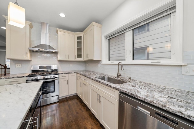 kitchen featuring dark wood-style floors, wall chimney exhaust hood, glass insert cabinets, stainless steel appliances, and a sink