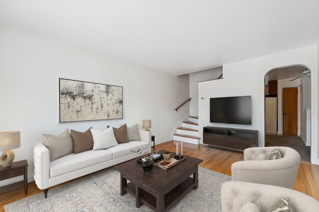 living room with arched walkways, stairway, and wood finished floors