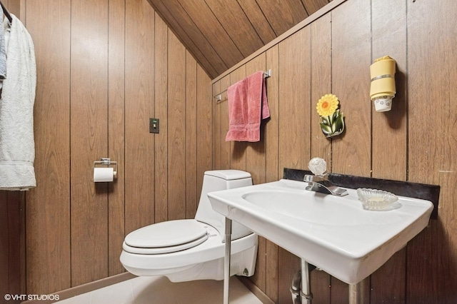 bathroom featuring toilet, tile patterned flooring, wooden walls, and a sink