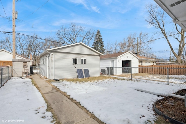 snow covered rear of property featuring a fenced backyard, a detached garage, and an outbuilding