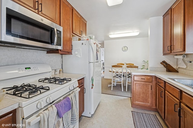 kitchen with white gas stove, stainless steel microwave, light countertops, and brown cabinets