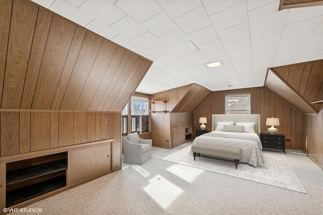 carpeted bedroom with lofted ceiling and wood walls