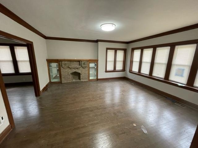 unfurnished living room with a brick fireplace, baseboards, ornamental molding, and wood finished floors