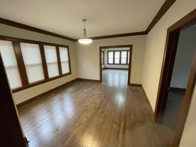 unfurnished dining area featuring crown molding, baseboards, and wood finished floors