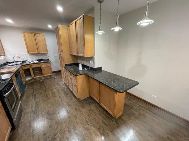 kitchen featuring a peninsula, tasteful backsplash, dark wood-style flooring, and gas range