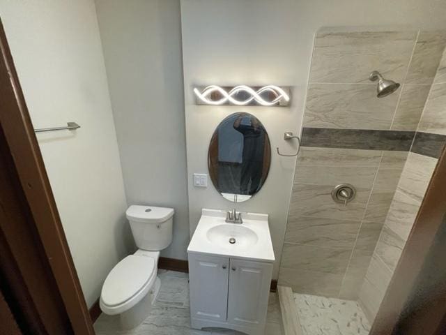 bathroom featuring toilet, baseboards, a tile shower, and vanity