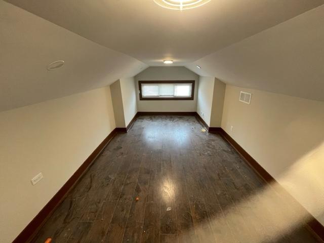 additional living space with dark wood-type flooring, visible vents, vaulted ceiling, and baseboards