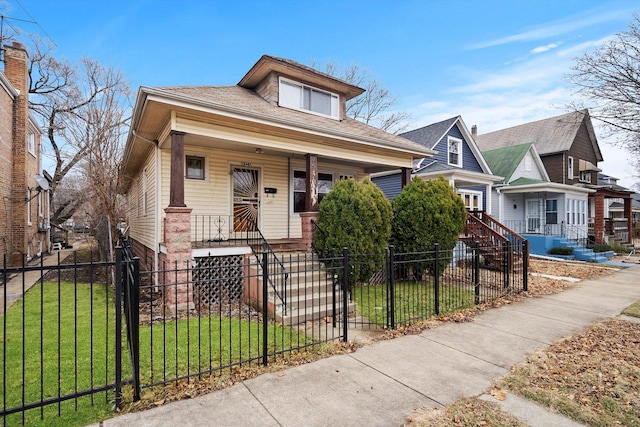 bungalow-style home with a fenced front yard, covered porch, and a front lawn