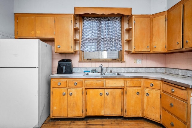 kitchen with open shelves, tasteful backsplash, light countertops, freestanding refrigerator, and a sink