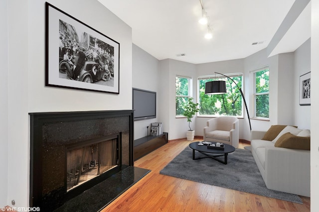 living room featuring rail lighting, visible vents, a fireplace, and wood finished floors