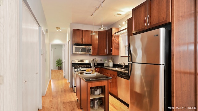 kitchen with light wood-style flooring, a kitchen island, a sink, appliances with stainless steel finishes, and pendant lighting