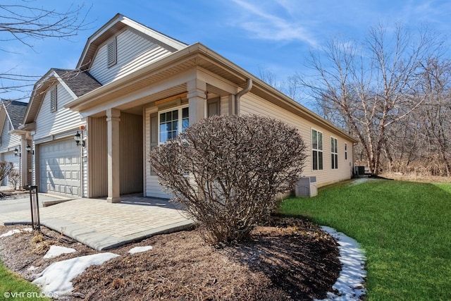 view of side of home featuring roof with shingles, a yard, central AC, a garage, and driveway