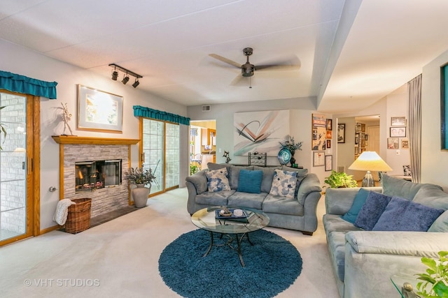 living area featuring visible vents, carpet flooring, ceiling fan, a stone fireplace, and track lighting