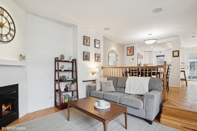 living area featuring visible vents, a fireplace, light wood-style flooring, and baseboards