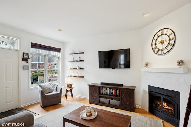 living room featuring baseboards, a tiled fireplace, and wood finished floors