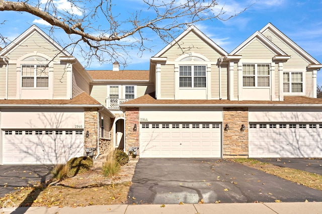 townhome / multi-family property featuring aphalt driveway, an attached garage, and stone siding