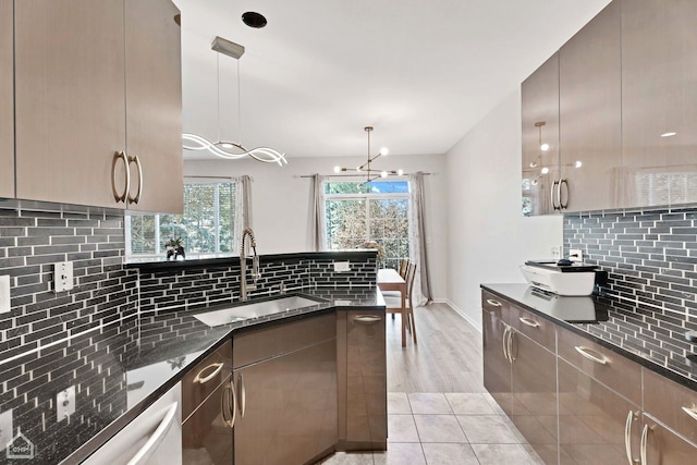 kitchen with dark stone countertops, a peninsula, backsplash, and a sink