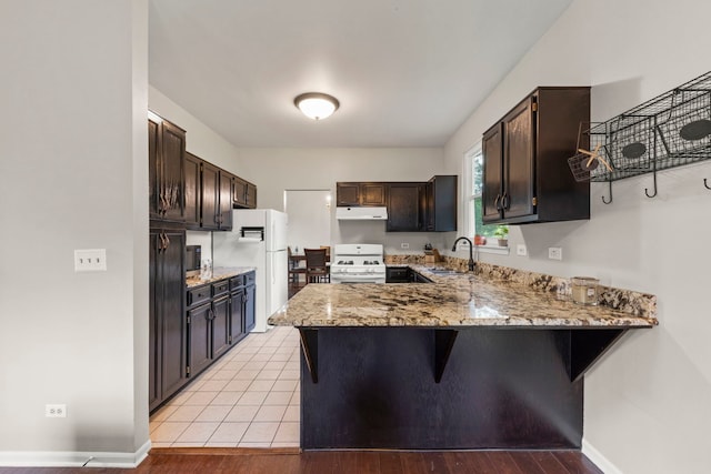 2031 Edinburgh Ln, Aurora, IL 60504 - kitchen with white appliances, a peninsula, under cabinet range hood, light stone counters, and dark brown cabinetry
