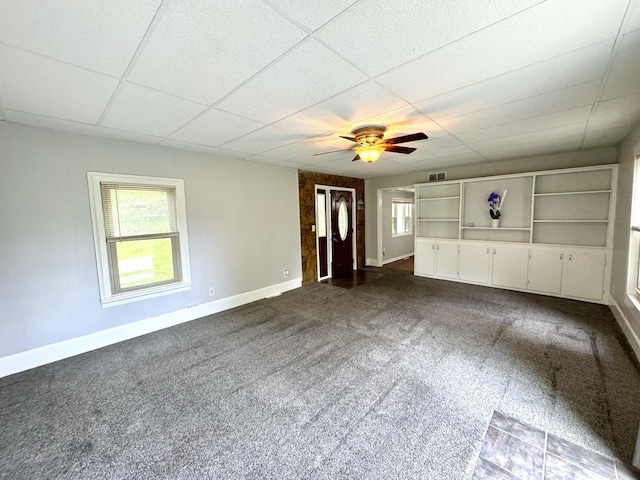 unfurnished living room featuring plenty of natural light, a ceiling fan, baseboards, and dark colored carpet