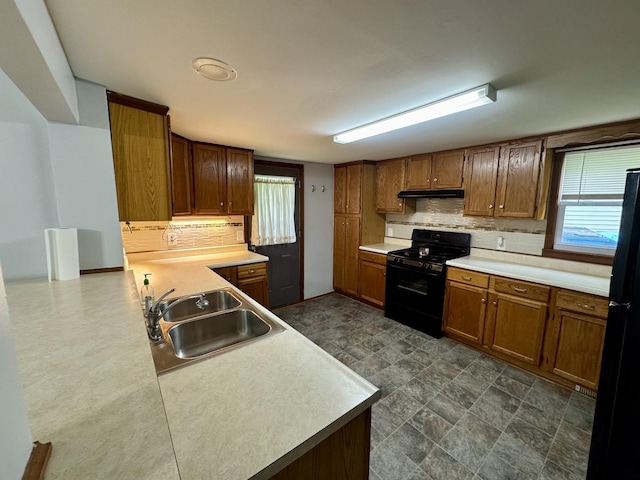 kitchen featuring backsplash, brown cabinets, a sink, black appliances, and under cabinet range hood