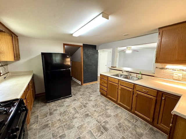 kitchen with a sink, light countertops, brown cabinetry, baseboards, and black appliances
