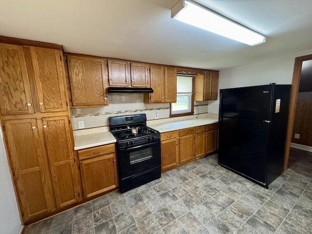 kitchen with tasteful backsplash, brown cabinets, light countertops, black appliances, and under cabinet range hood
