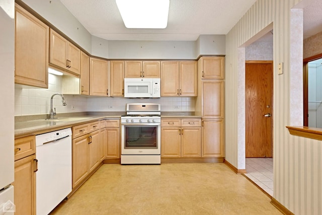 kitchen with a sink, white appliances, wallpapered walls, and light brown cabinetry