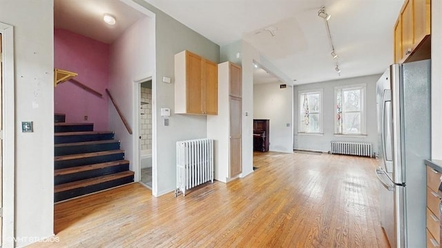 unfurnished living room featuring radiator, light wood-style floors, stairway, and rail lighting