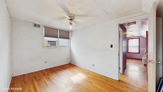 empty room with radiator, ceiling fan, visible vents, and wood finished floors