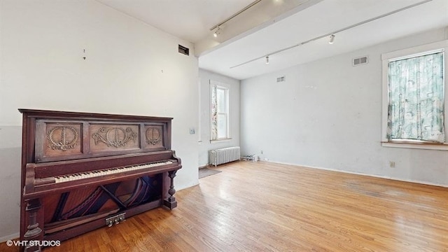 living area with radiator heating unit, light wood-type flooring, visible vents, and track lighting