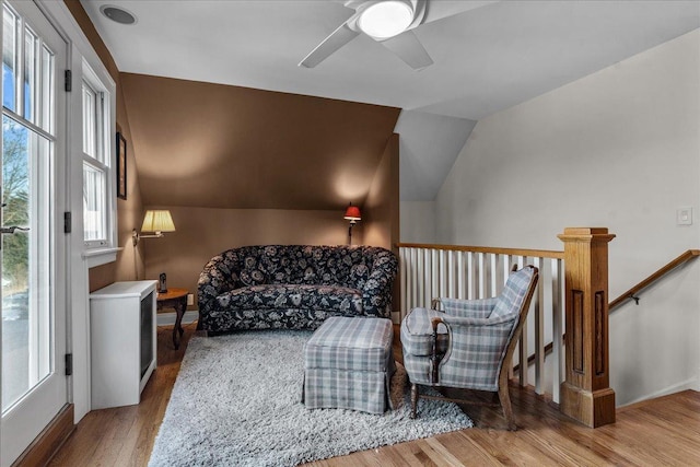 living area with wood finished floors, baseboards, ceiling fan, vaulted ceiling, and an upstairs landing