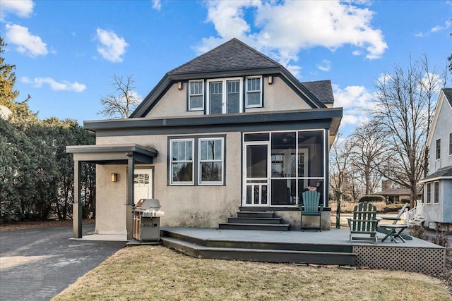 rear view of house featuring a shingled roof, a sunroom, stucco siding, a yard, and a deck