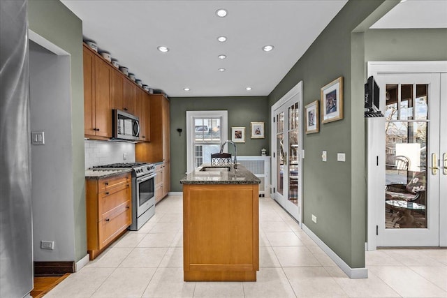 kitchen featuring tasteful backsplash, an island with sink, dark stone countertops, stainless steel appliances, and a sink