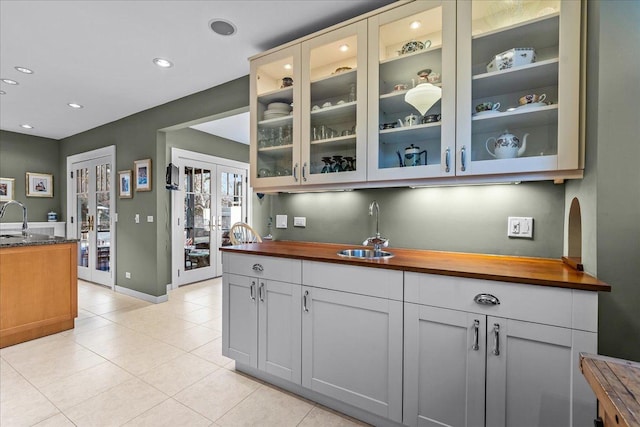 interior space featuring a sink, wood counters, glass insert cabinets, and light tile patterned flooring