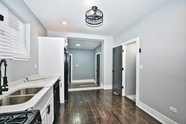 kitchen featuring dark wood-type flooring, a sink, white cabinetry, baseboards, and black dishwasher