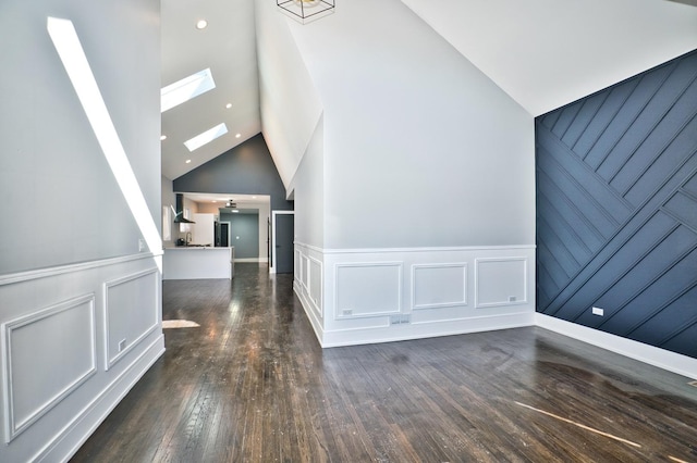 interior space with high vaulted ceiling, a skylight, a decorative wall, and hardwood / wood-style floors