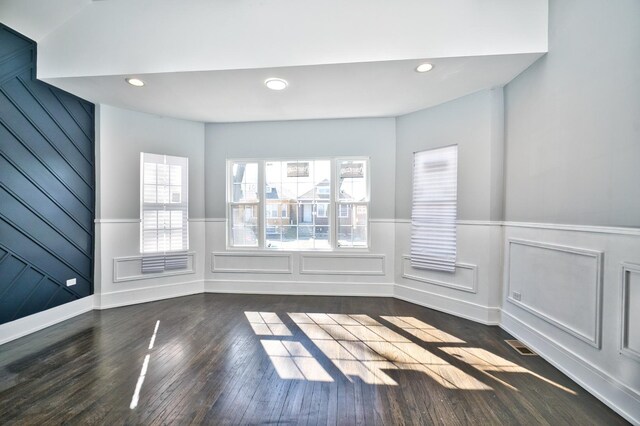 empty room featuring dark wood-type flooring, wainscoting, visible vents, and recessed lighting